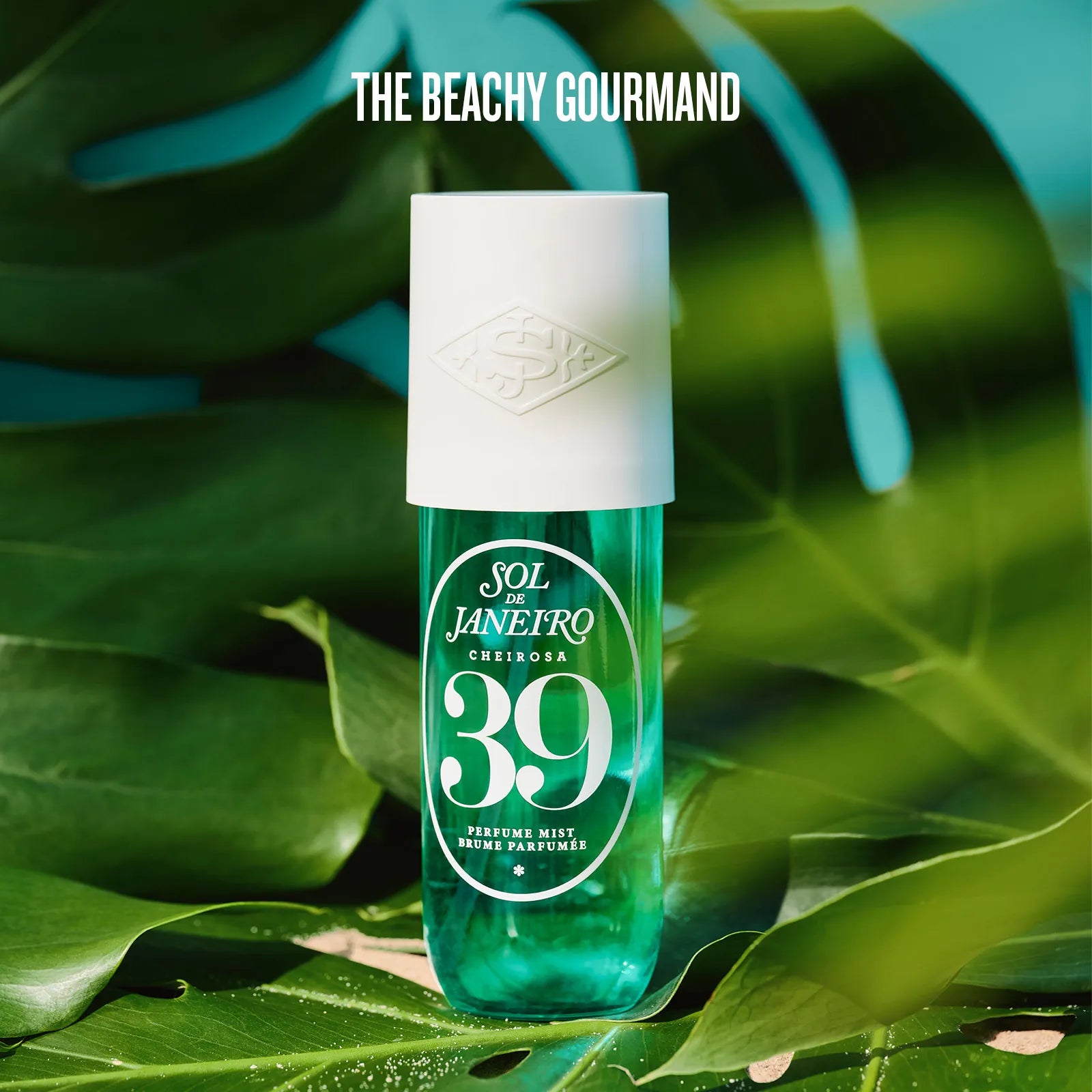 Green perfume bottle with white cap on green leaves, 'The Beachy Gourmand' branding.