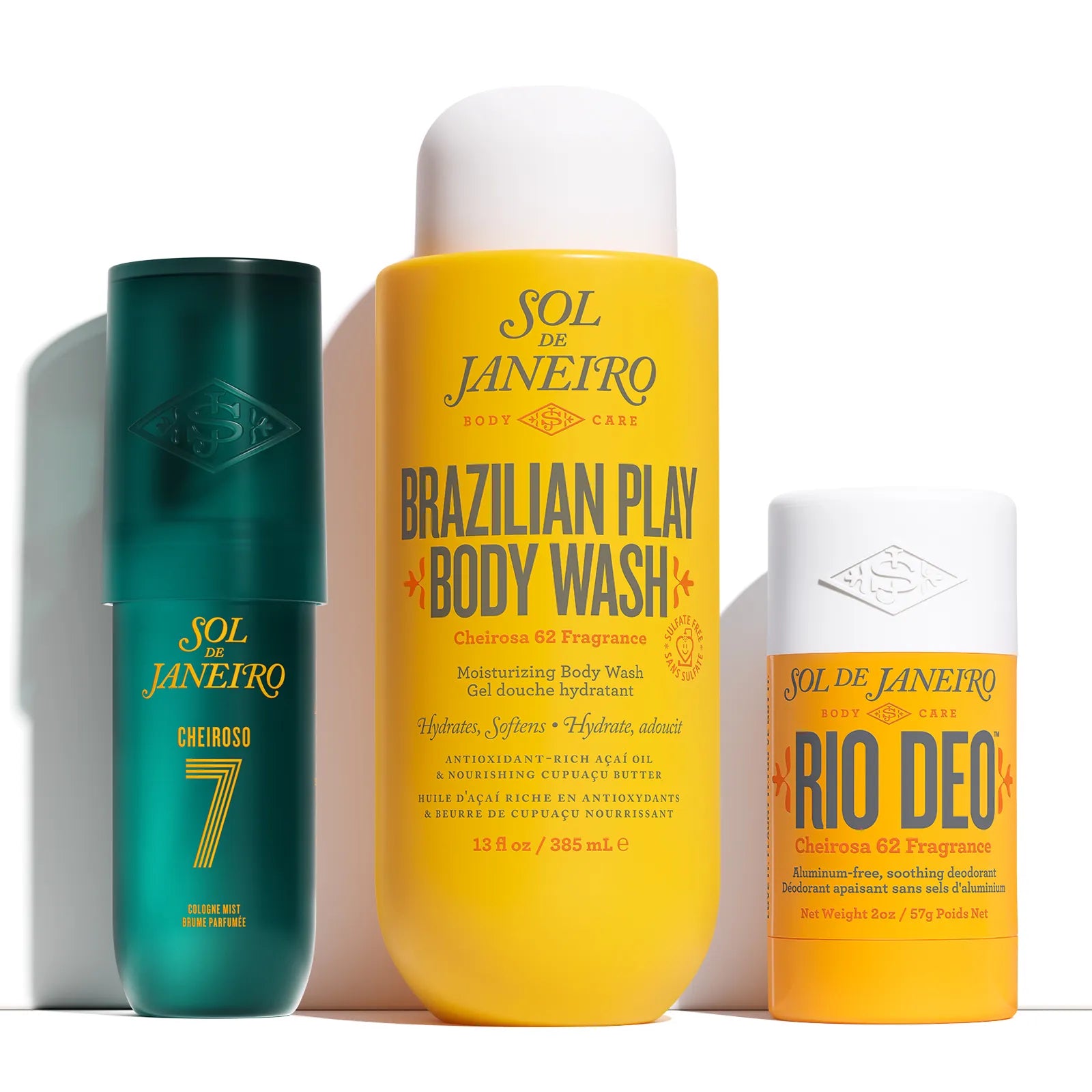 Three Sol de Janeiro body care products on a white background: a teal body wash bottle labeled Cheiroso 7, a large yellow body wash bottle labeled Brazilian Play Body Wash, and an orange deodorant stick labeled Rio Deo.